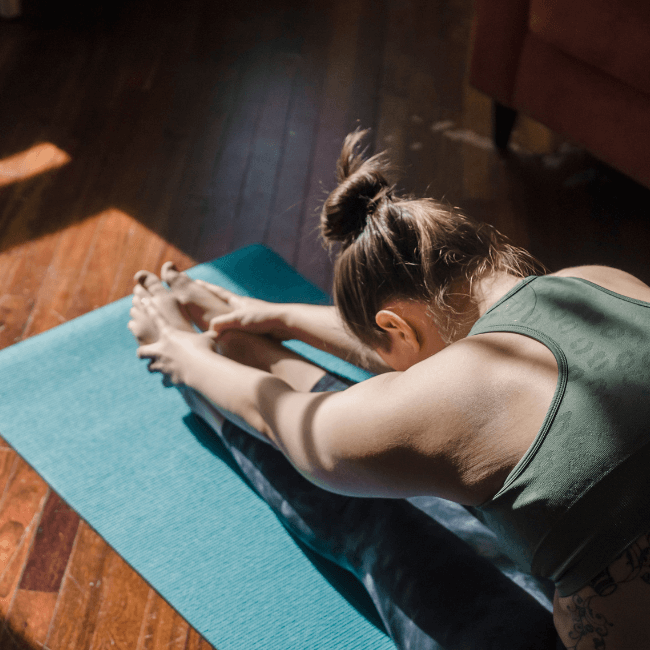 A Woman Is Sitting On A Yoga Mat Stretching Her Legs — Howells & Co Legal & Conveyancing In Lake Cessnock, NSW
