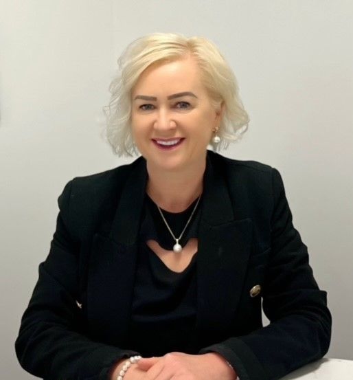 A Woman With Blonde Hair Is Wearing A White Jacket And Smiling — Howells & Co Legal & Conveyancing In Gosford, NSW