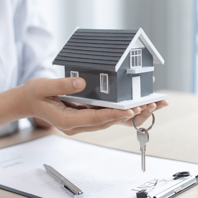 A Person Is Holding A Model House And Keys In Their Hands — Howells & Co Legal & Conveyancing In Lake Cessnock, NSW