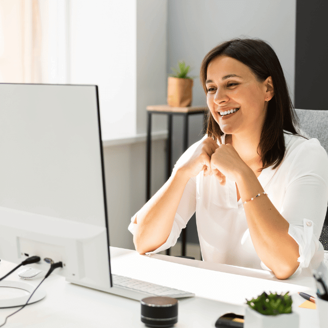 A Woman Is Sitting At A Desk In Front Of A Computer And Smiling — Howells & Co Legal & Conveyancing In Cessnock, NSW
