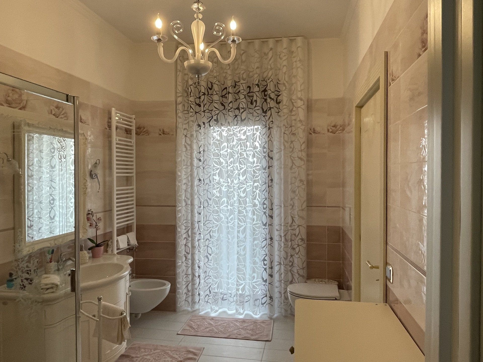 Un bagno con lavandino, water, specchio e lampadario.