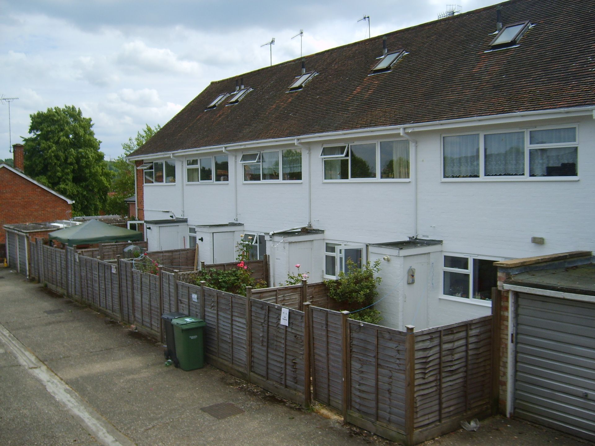 Row of white townhouses with brown roofs and wooden fences, seen from an elevated perspective on a cloudy day.