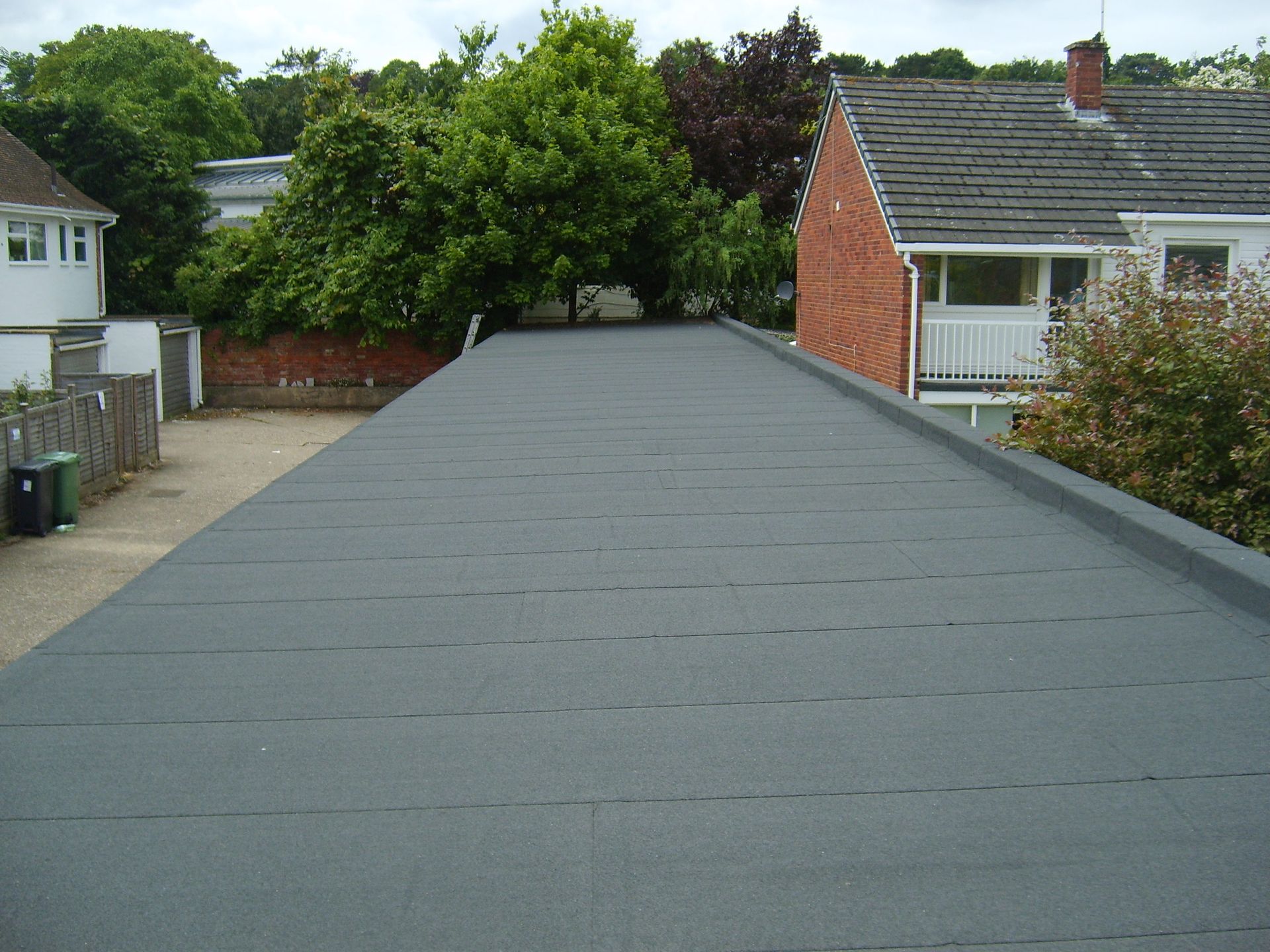 A gray flat roof on a residential building with trees and other houses in the background.