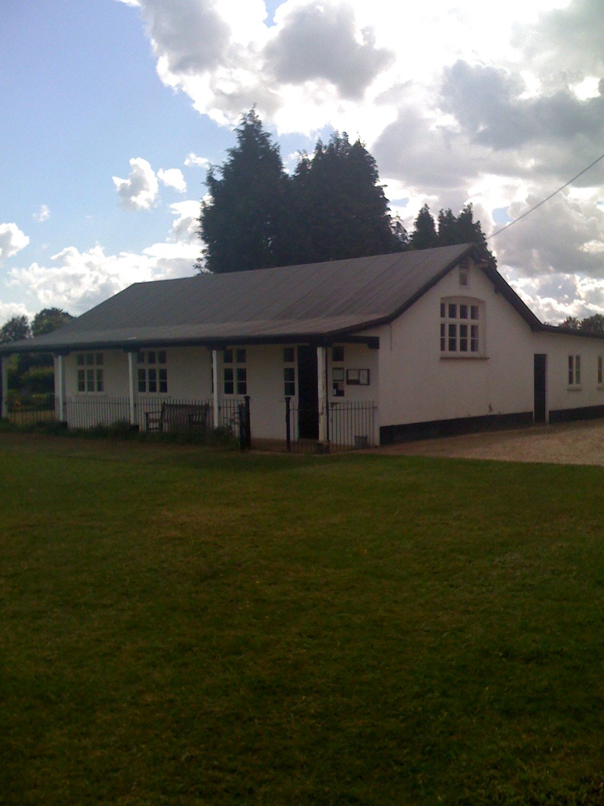 A white, single-story building with a dark roof on a grassy field under a cloudy sky.