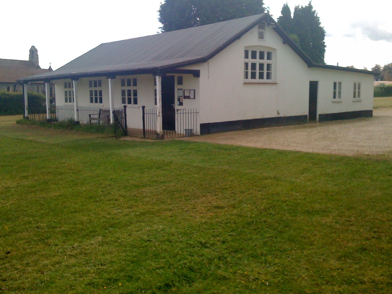 White cricket pavilion on a green lawn, with a gray roof and a small extension.