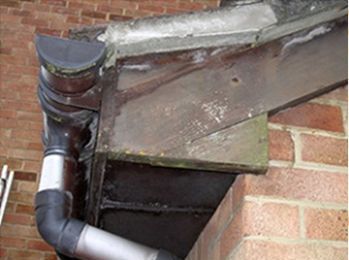 Damaged gutter and downspout attached to a brick building. The gutter is metal and the downspout is plastic.