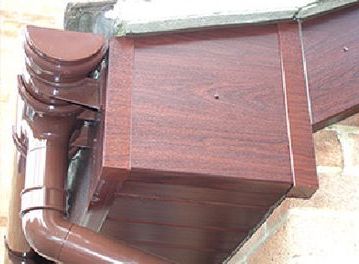 Brown gutter and downspout on a building, with a wooden facade visible.