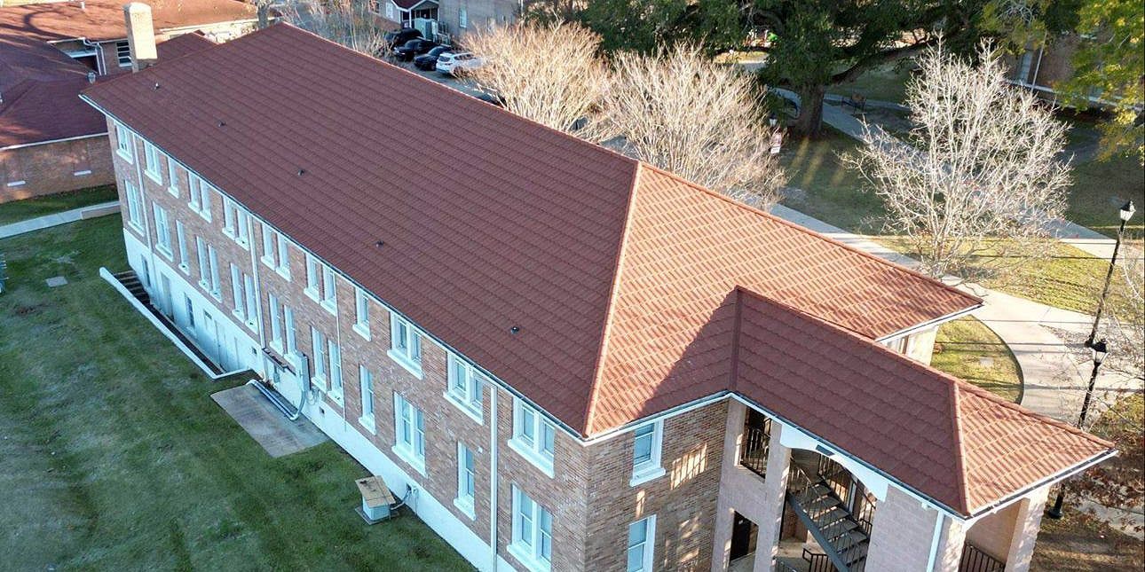 Aerial view of a three-story brick building with a brown tiled roof, situated on a green lawn.