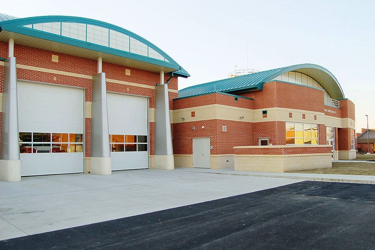 Fire station building with red brick exterior, teal roof accents, and two large garage doors.
