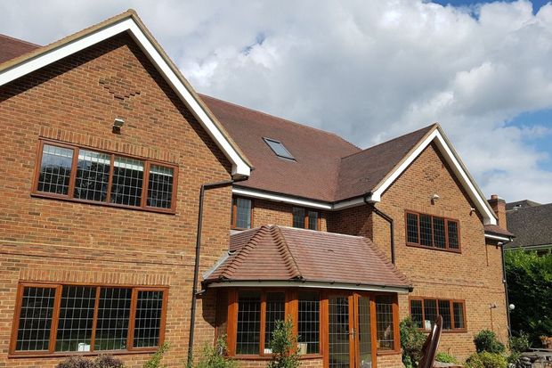 Two-story brick house with brown trim, windows, and tiled roof; blue sky with clouds in background.