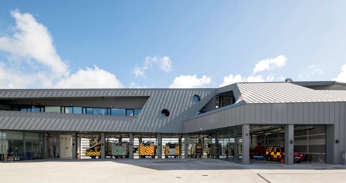 Modern fire station with several emergency vehicles parked inside the open bay doors under a blue sky.