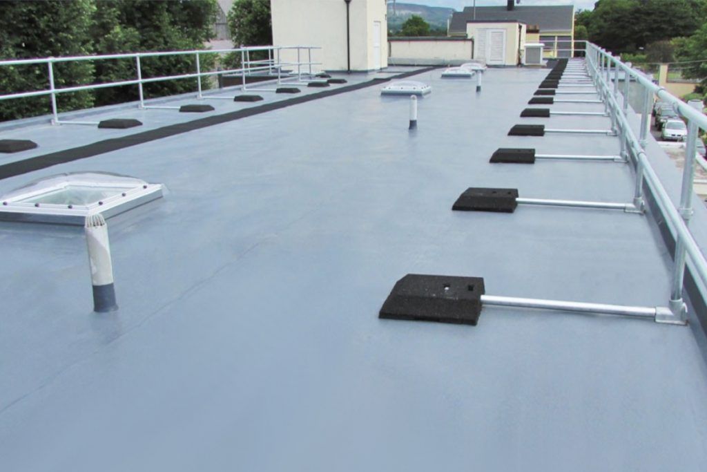Flat, gray commercial rooftop with safety railing. Features several equipment mounts and ventilation pipes.