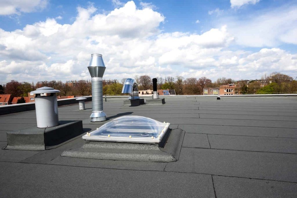 Flat, black rooftop with various ventilation units and a skylight against a cloudy sky.