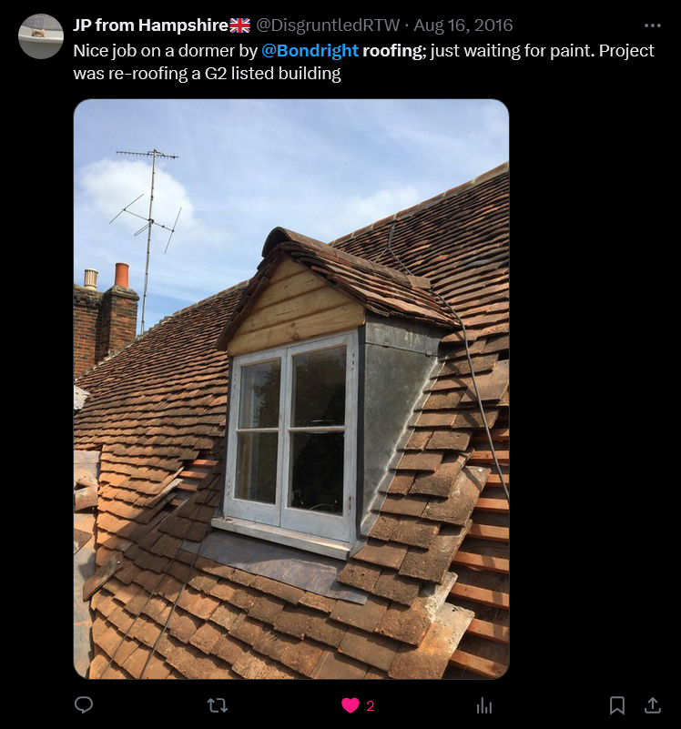 Dormer window on a roof of a building being re-roofed. Brown roof tiles, with a white window frame.