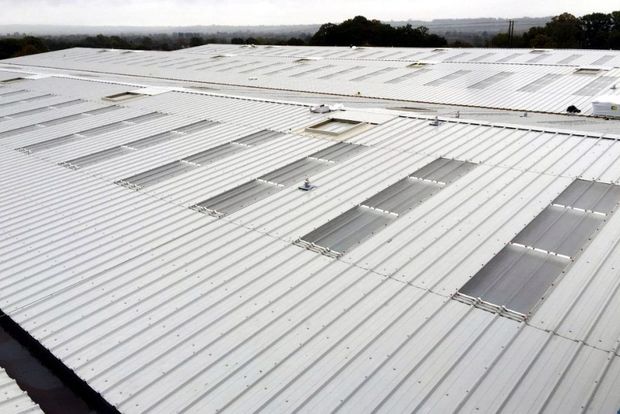 Aerial view of a large white industrial building roof with evenly spaced light panels.