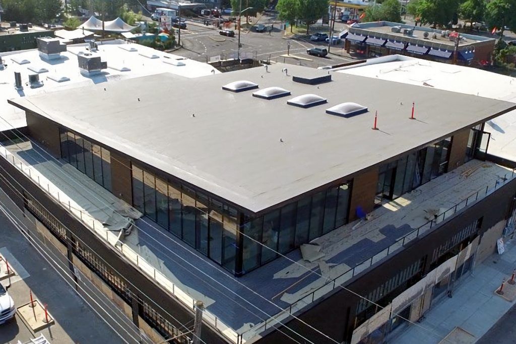 Aerial view of a modern building with a flat grey roof and large glass windows.