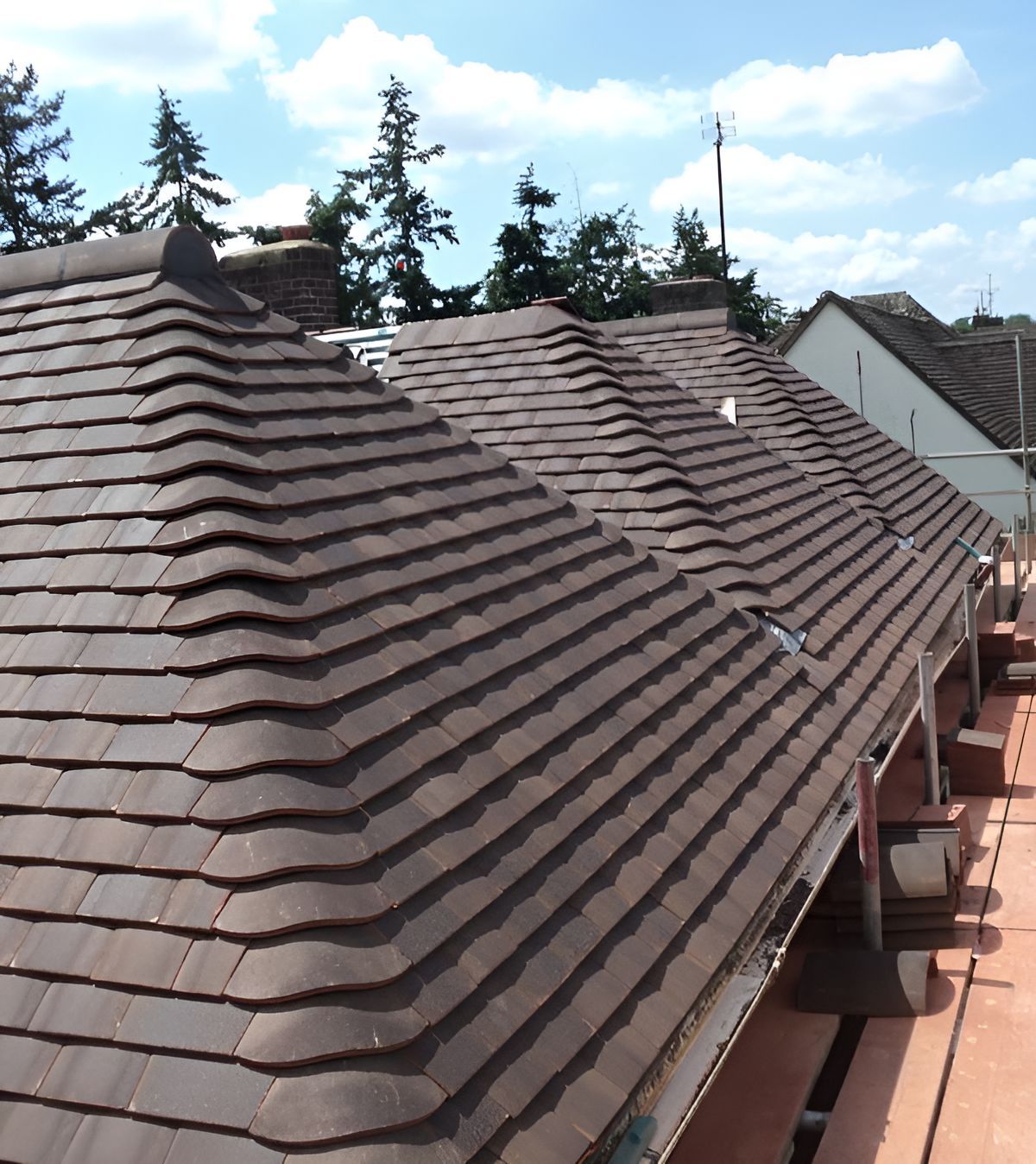 Brown tiled roof with a wavy design, under a blue sky with some trees.