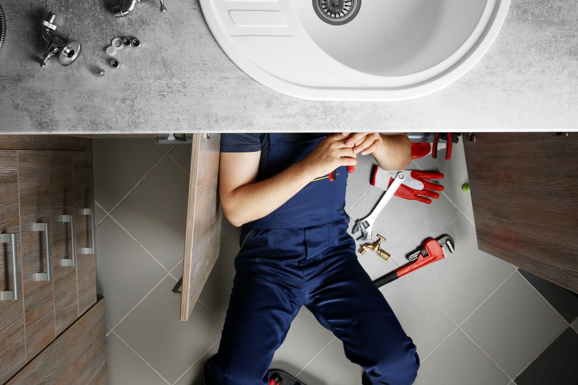 A plumber repairing pipes under the bathroom sink with tools nearby.