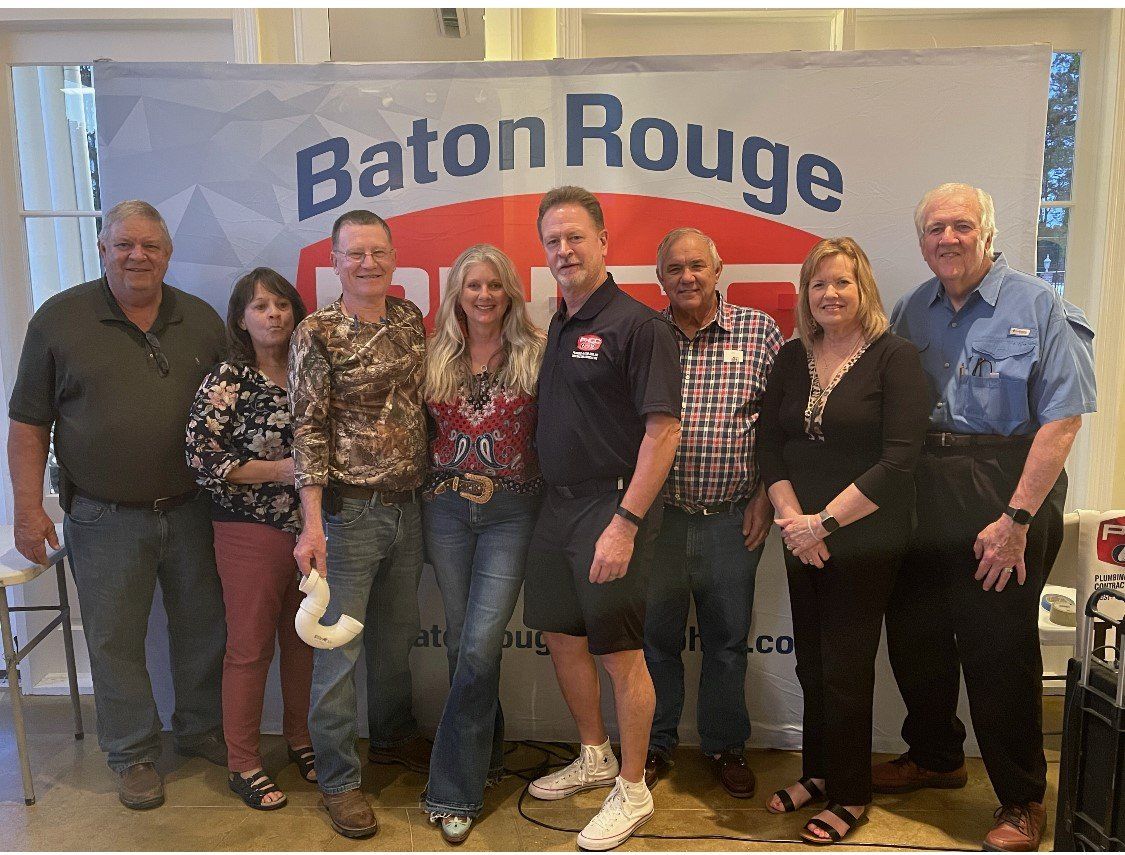 Group of nine people smiling in front of a Baton Rouge banner.