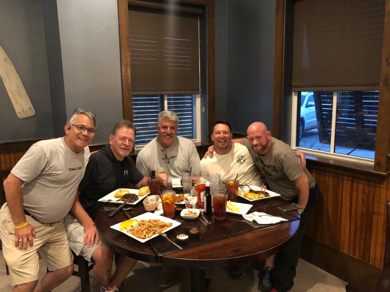 Five men smiling at a table in a restaurant, plates of food in front of them.