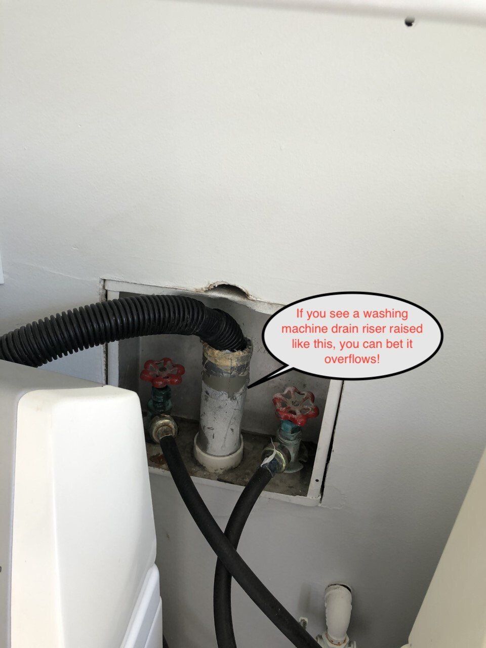 White washing machine water hookup with red shutoff valves and a drain hose.