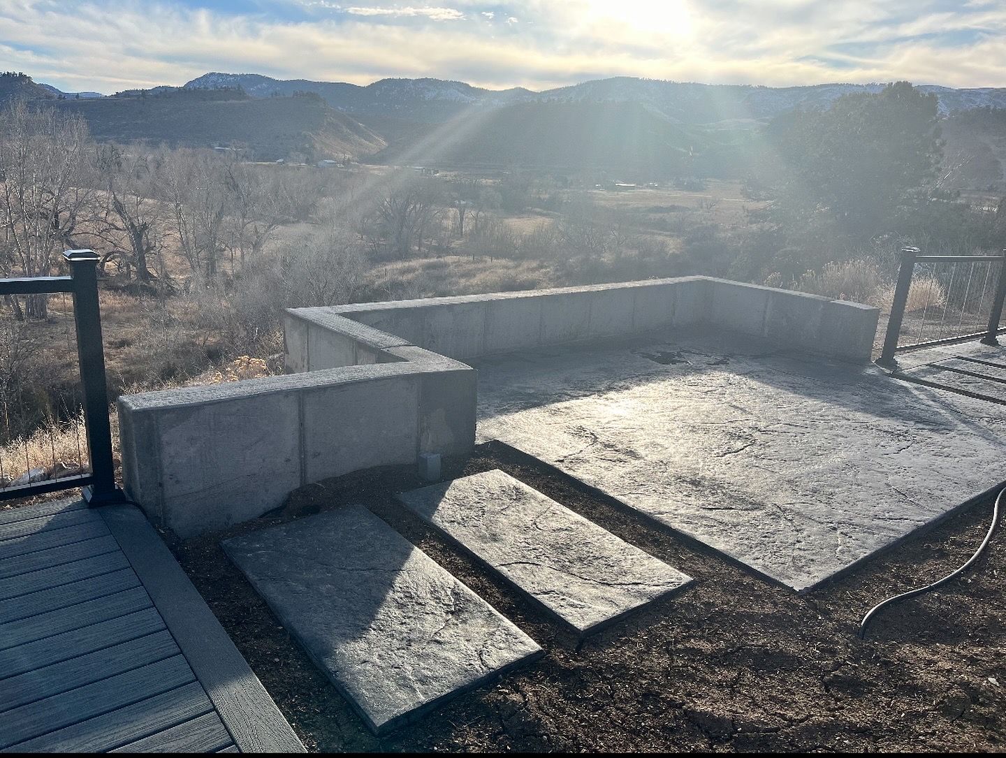 Patio with concrete walls and steps overlooking a mountain landscape under a bright sky.