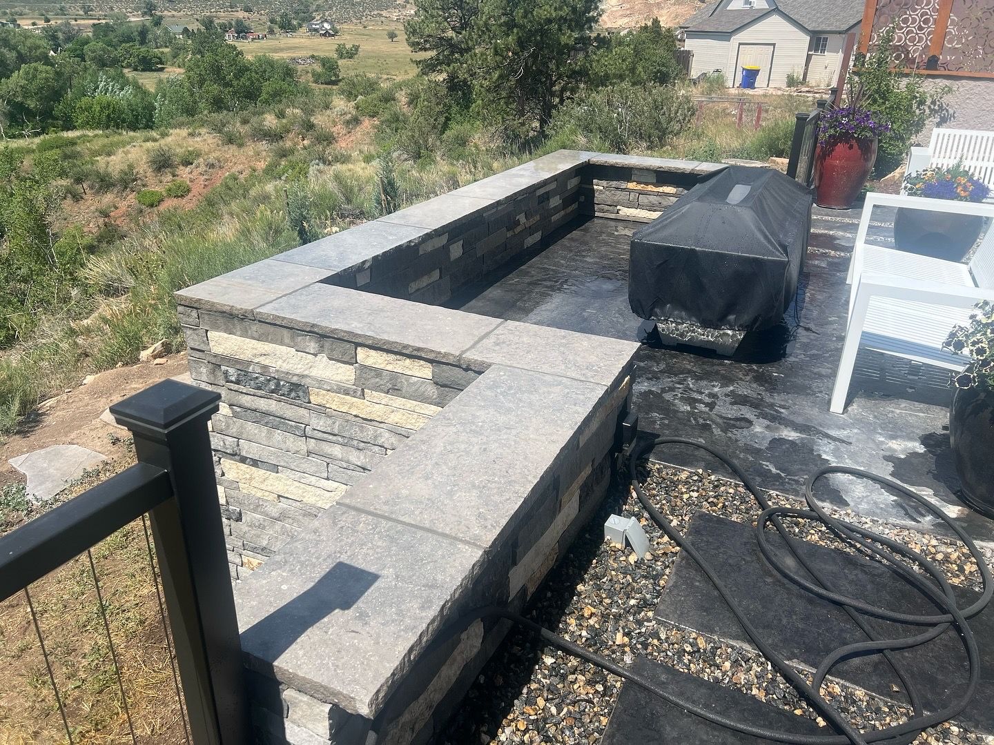 Outdoor patio with a stone fire pit, dark railing, and a hillside view.