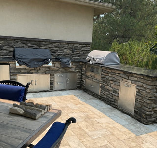 Outdoor kitchen with stainless steel grill, cabinets, and reddish stone counters and flooring.