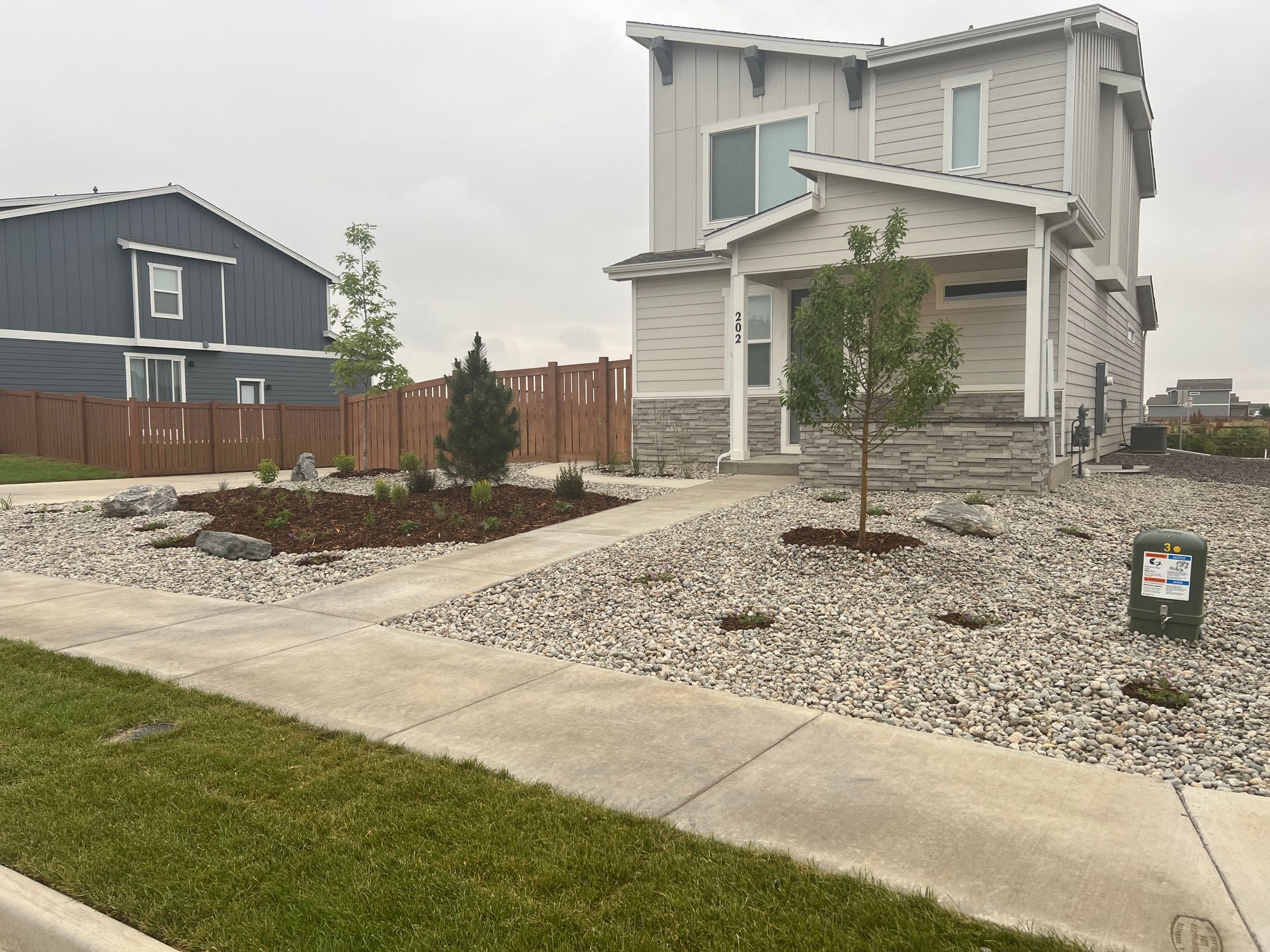 Two-story house with gravel landscaping, a small tree, and a wooden fence on a cloudy day.
