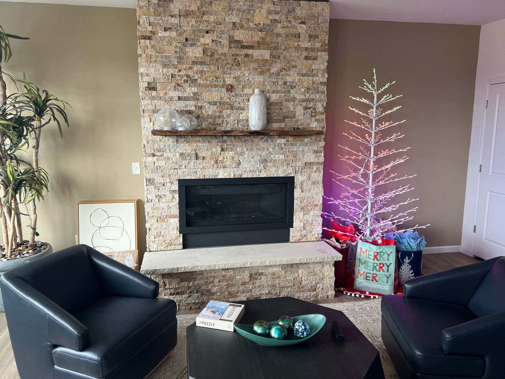 Living room with stone fireplace, chairs, and a lighted Christmas tree.