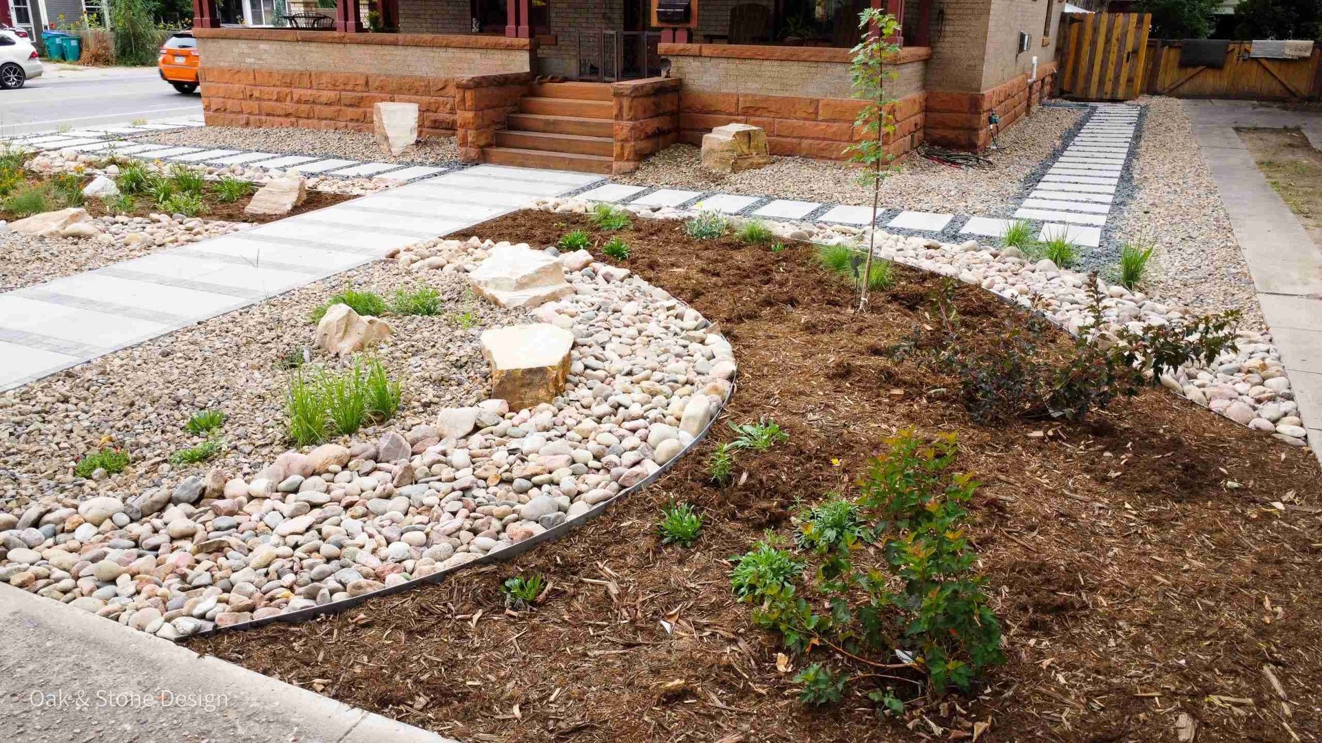 Landscaped front yard with stone paths, mulch, and river rock border.