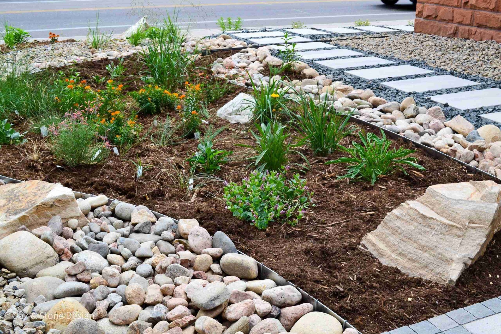 Landscaped garden bed with plants, rocks, and a stone walkway.