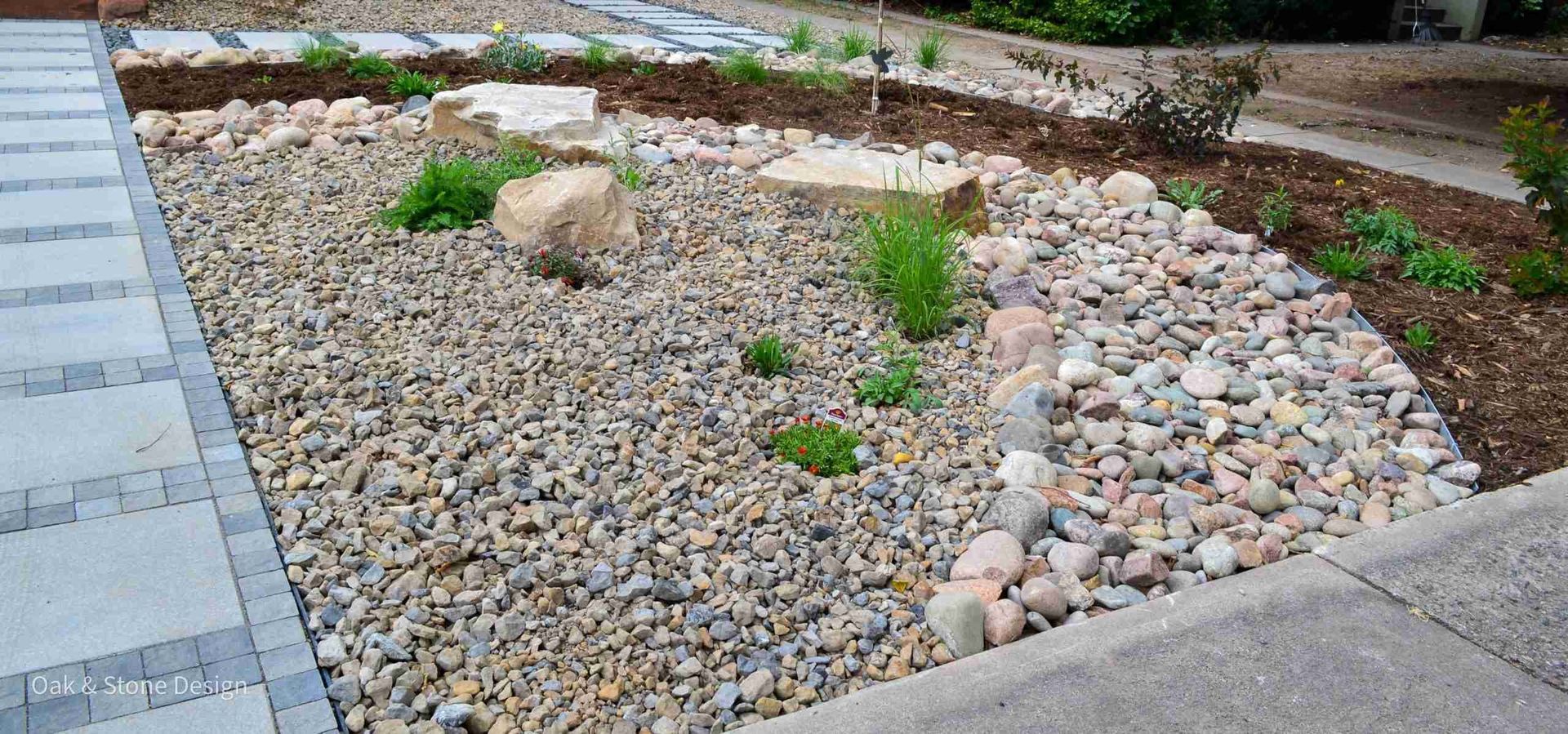 A gravel garden bed with rocks, plants, and a paved walkway.