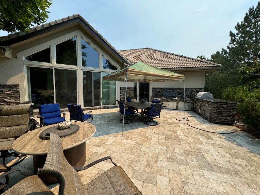 Patio with seating, round tables, outdoor kitchen, and a tent-like shelter under a sunny sky.