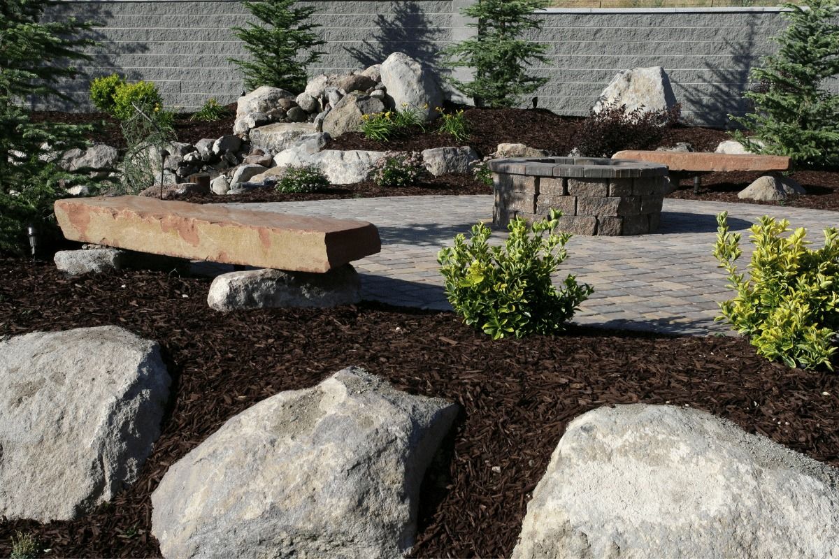 Landscaped patio with fire pit, stone benches, rocks, and mulch.