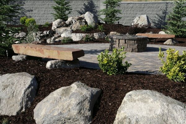 Landscaped patio with fire pit, stone benches, rocks, and mulch.