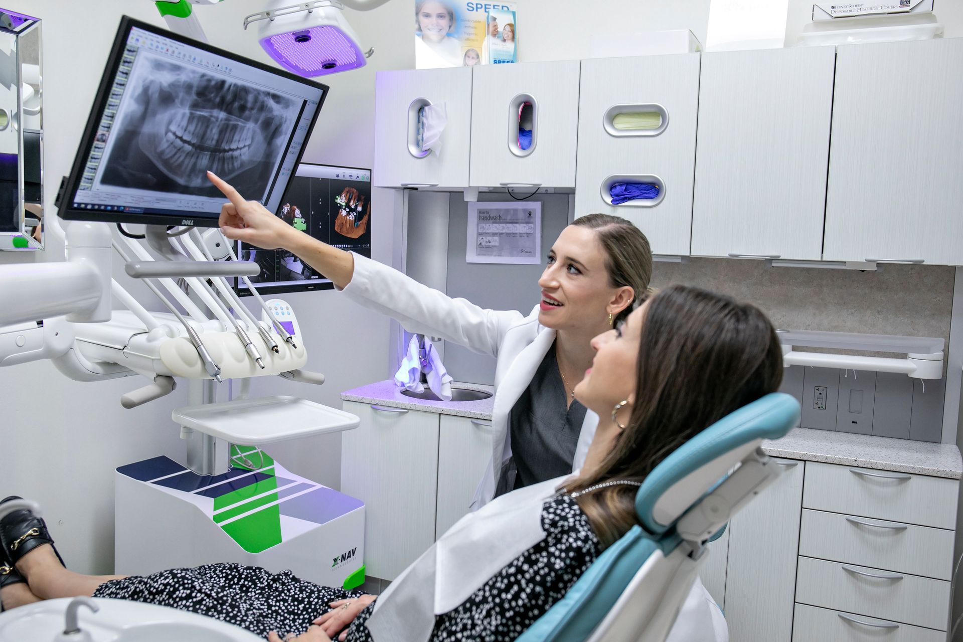 A woman is sitting in a dental chair looking at an x-ray.