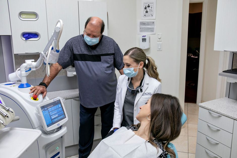 A man and a woman are standing next to a woman in a dental chair.