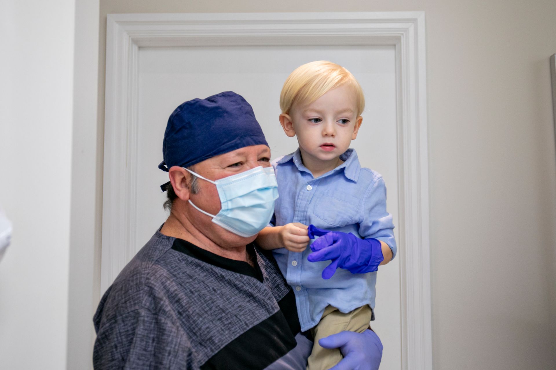 A woman wearing glasses and a blue scrub top is smiling for the camera.