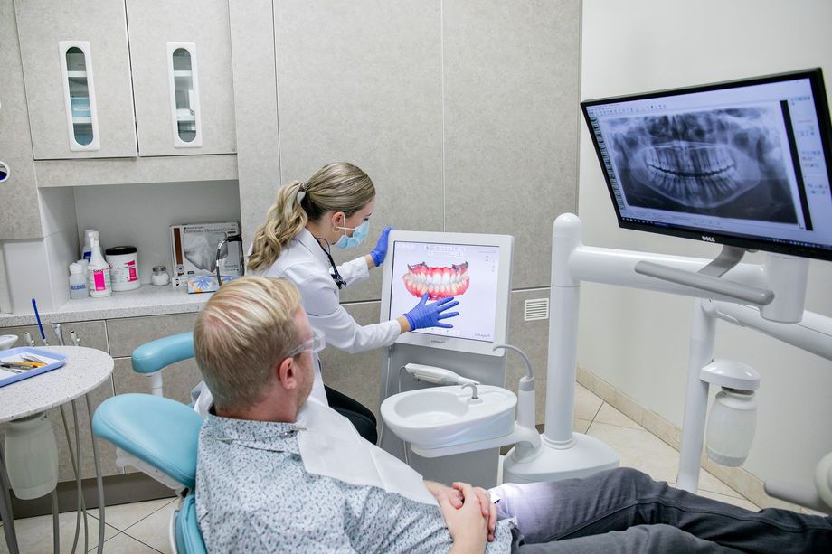 A man is sitting in a dental chair while a dentist examines his teeth.