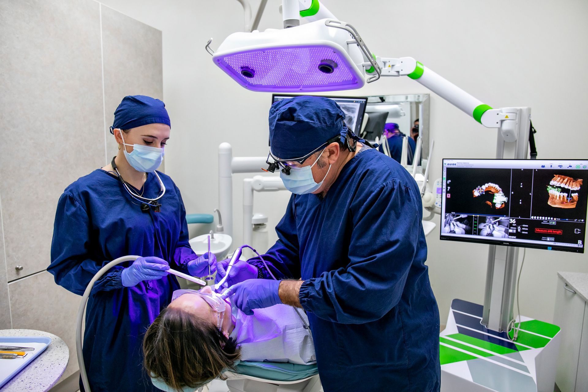 A man and a woman are working on a patient 's teeth in a dental office.