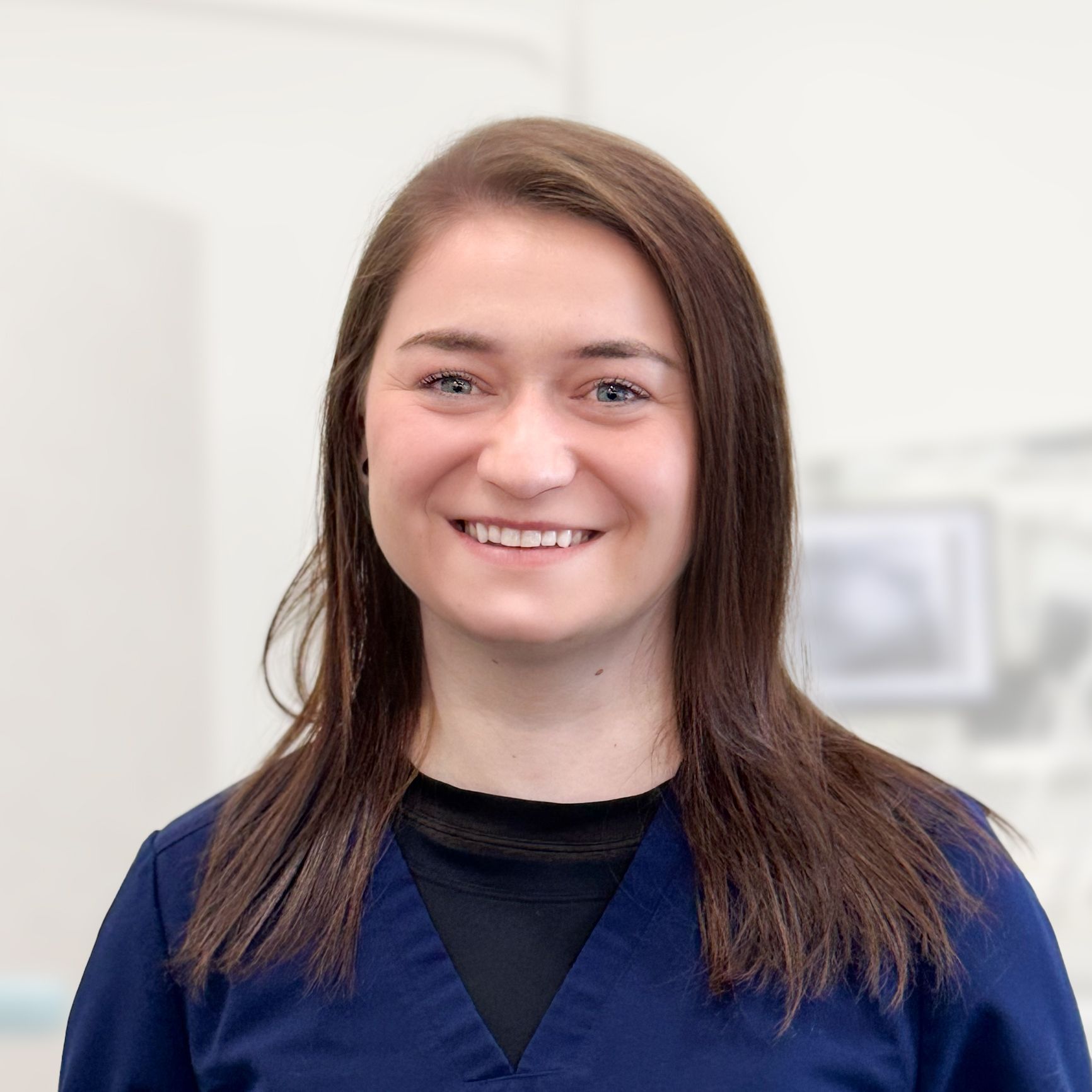 A woman in a blue scrub top is smiling for the camera.