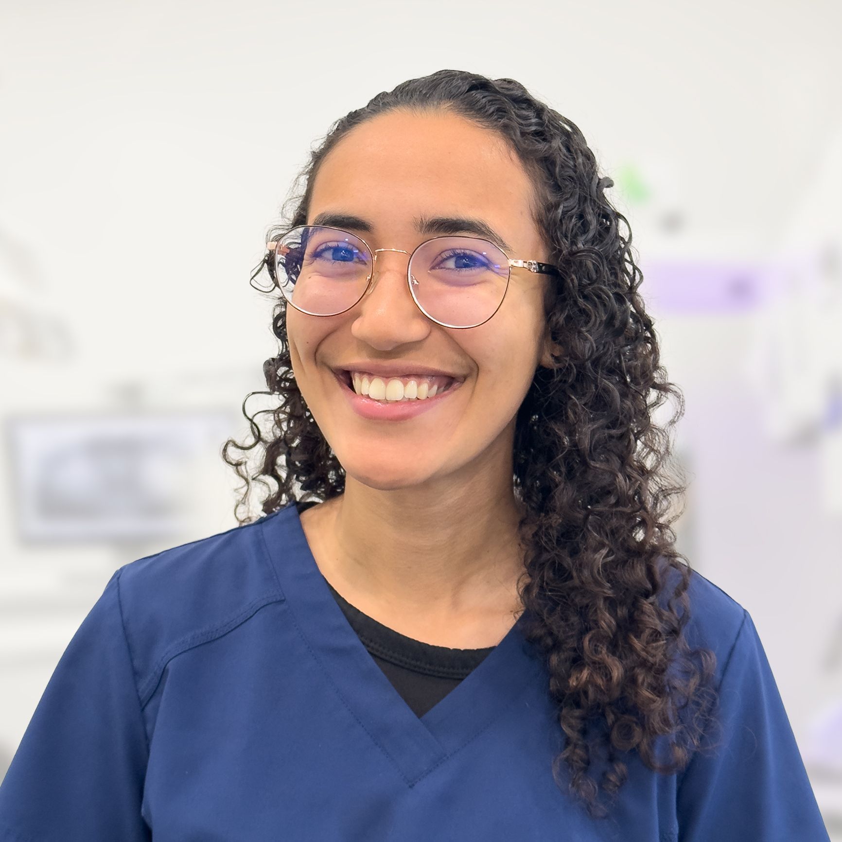 A woman wearing glasses and a blue scrub top is smiling for the camera.