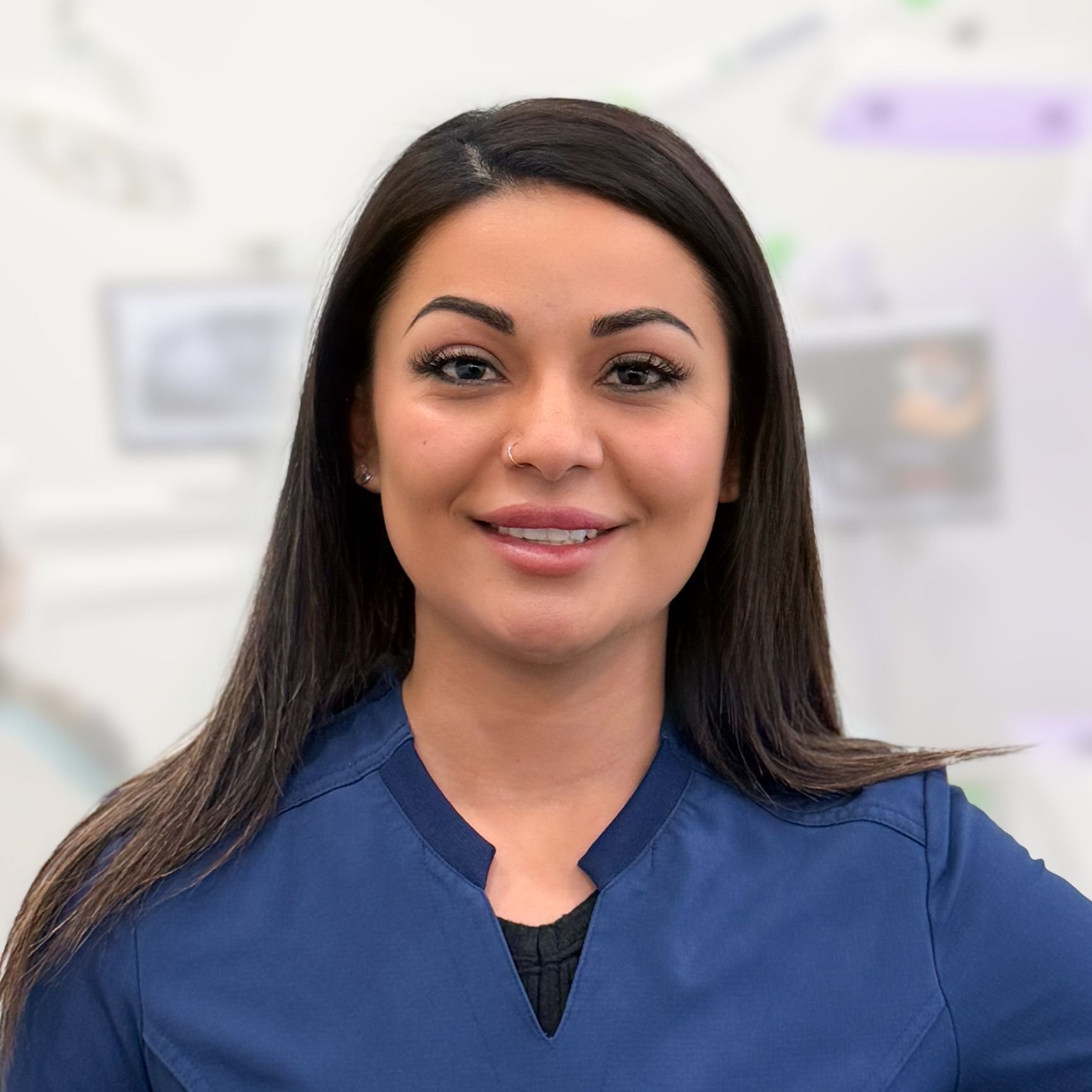 A woman in a blue scrub top is smiling for the camera.