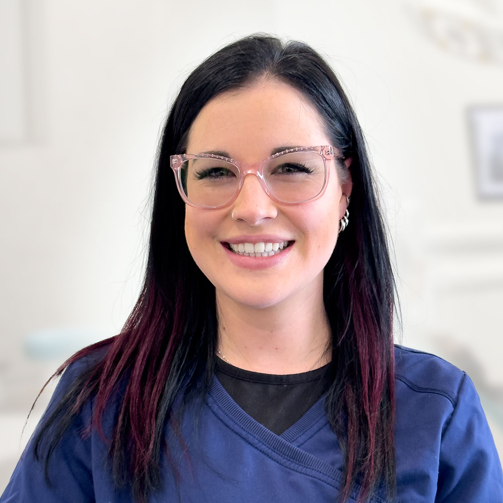 A woman wearing glasses and a blue scrub top is smiling for the camera.