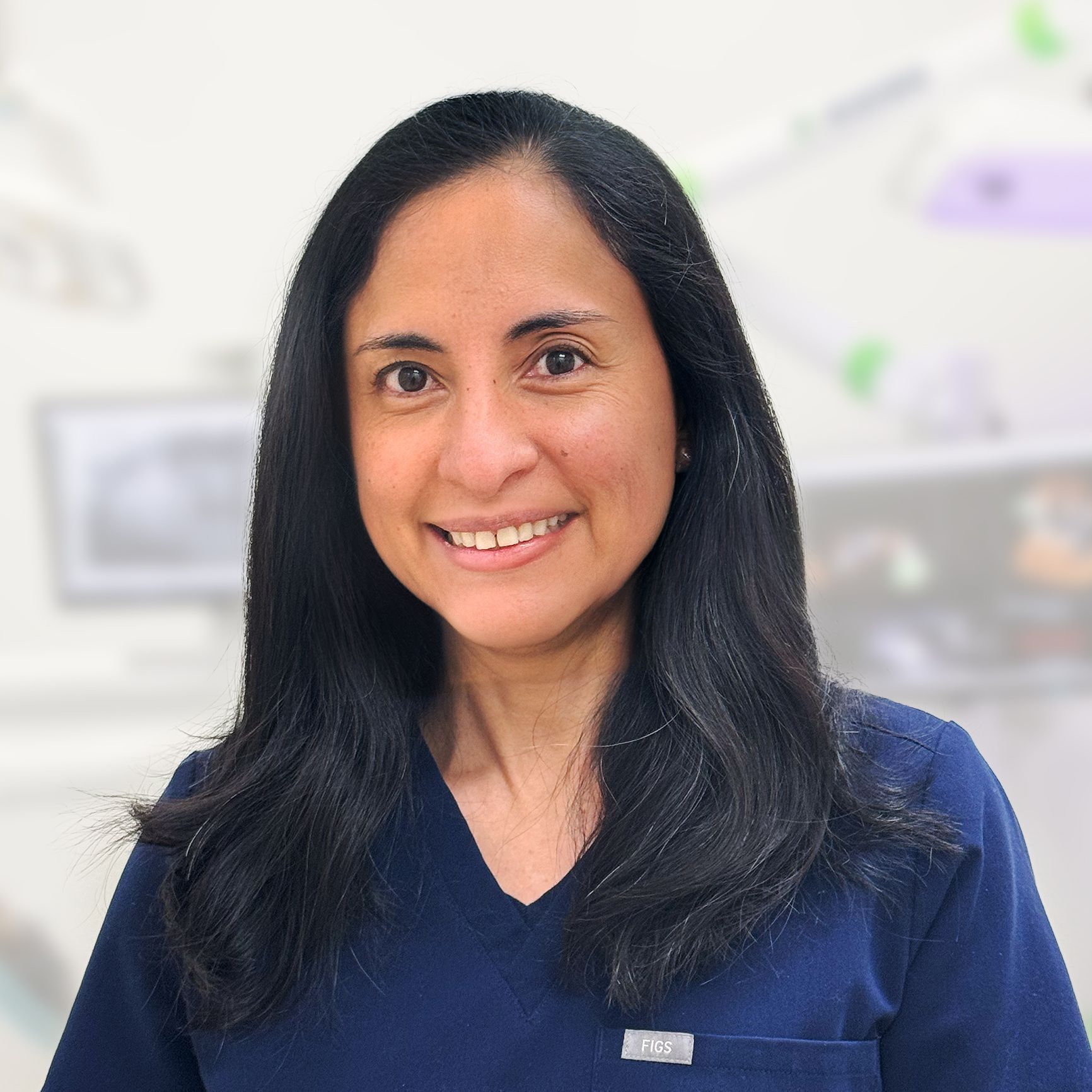 A woman in a blue scrub top is smiling for the camera.