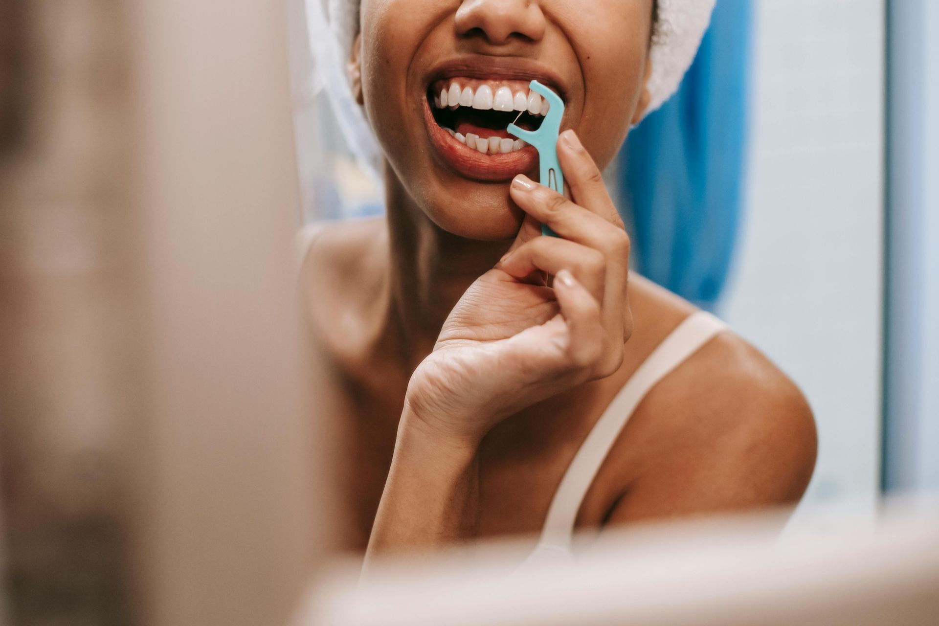 A woman is brushing her teeth with a floss in front of a mirror.