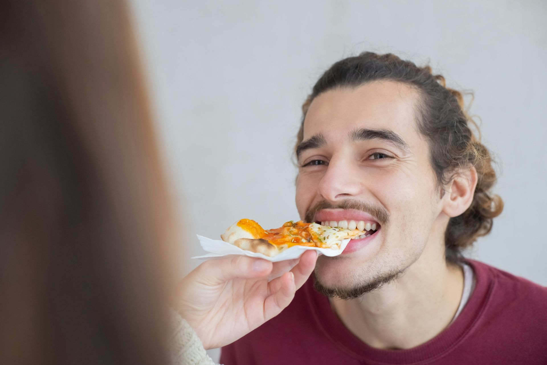 A man is eating a slice of pizza from a woman 's hand.