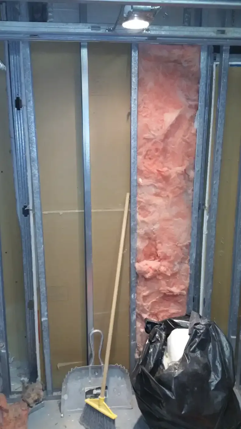 A broom and shovel are sitting in front of a wall with insulation.