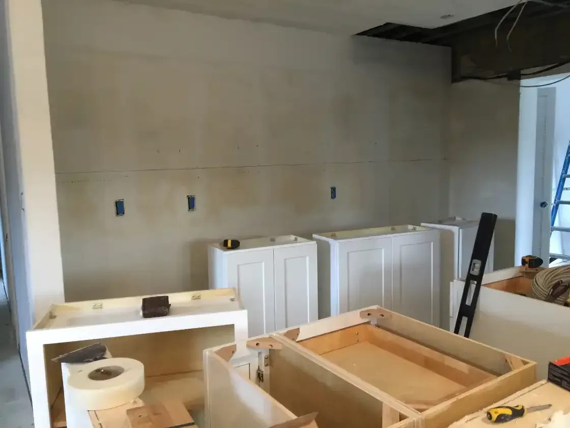 A kitchen under construction with white cabinets and a ladder.